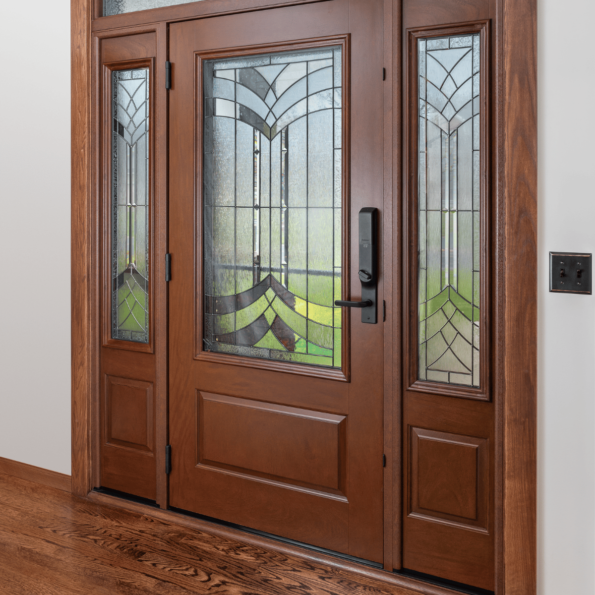 An Ensemble entry door with dual sidelights and artglass. The door and sidelight panel finish is a rich wood. There is black hardware.