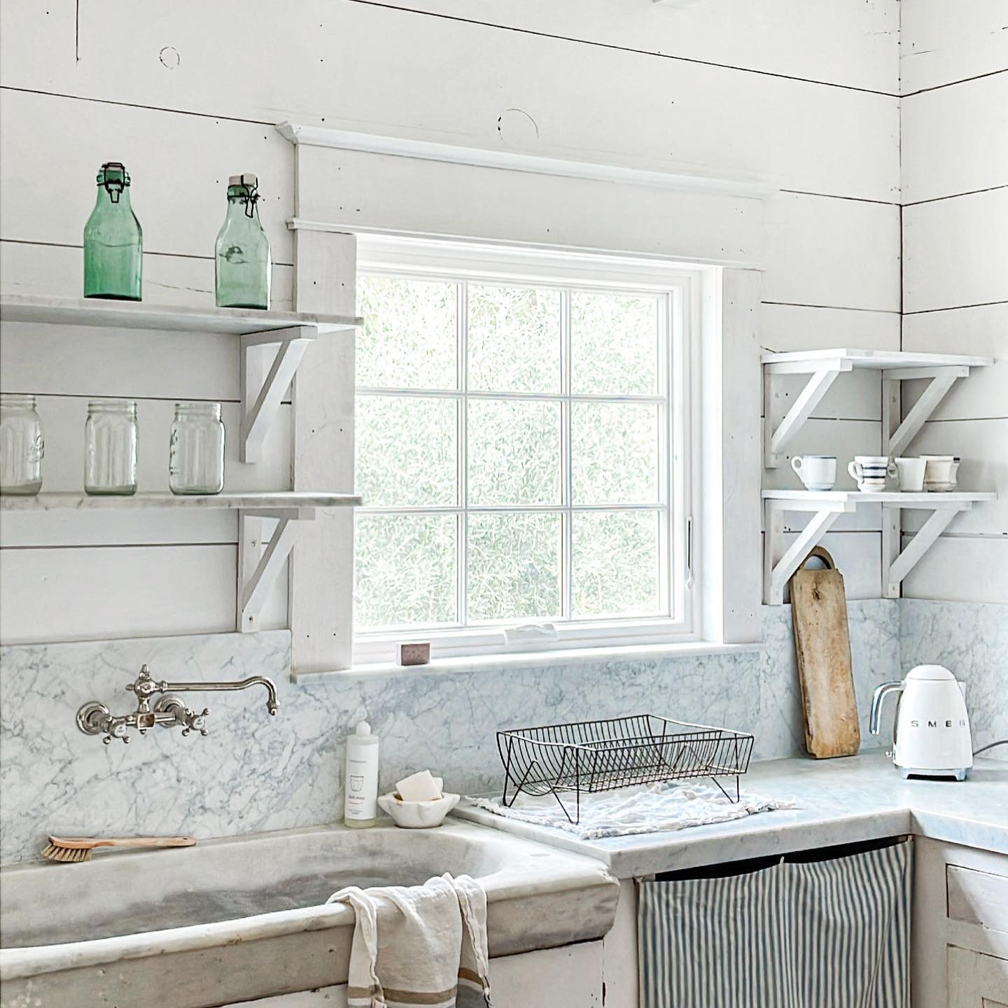 A white farmhouse kitchen with a casement window behind the sink. The window has colonial grilles.
