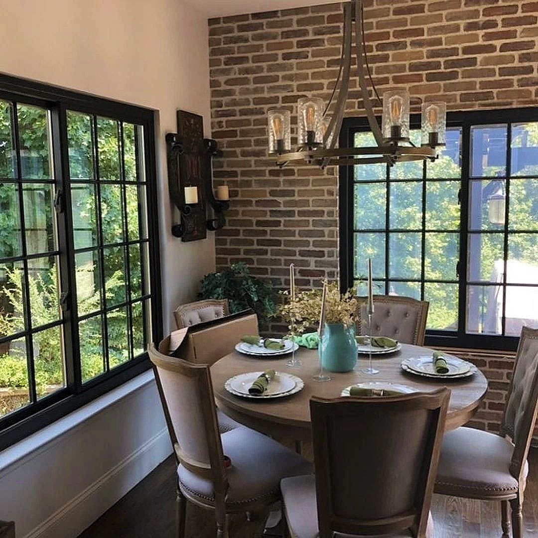 A dining area with gliding or sliding windows on either side of the table. The windows have black frames and colonial grilles.